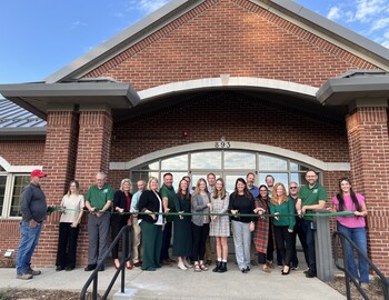 Representatives standing in front of building, preparing to cut the ribbon.