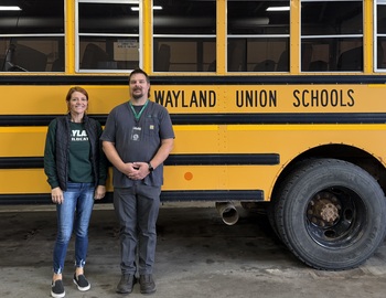 Karla Heckathorn (L) and John Syers (R) in front of a Wayland Union Schools bus. The coin is hanging from the lanyard on Mr. Syers’ neck.